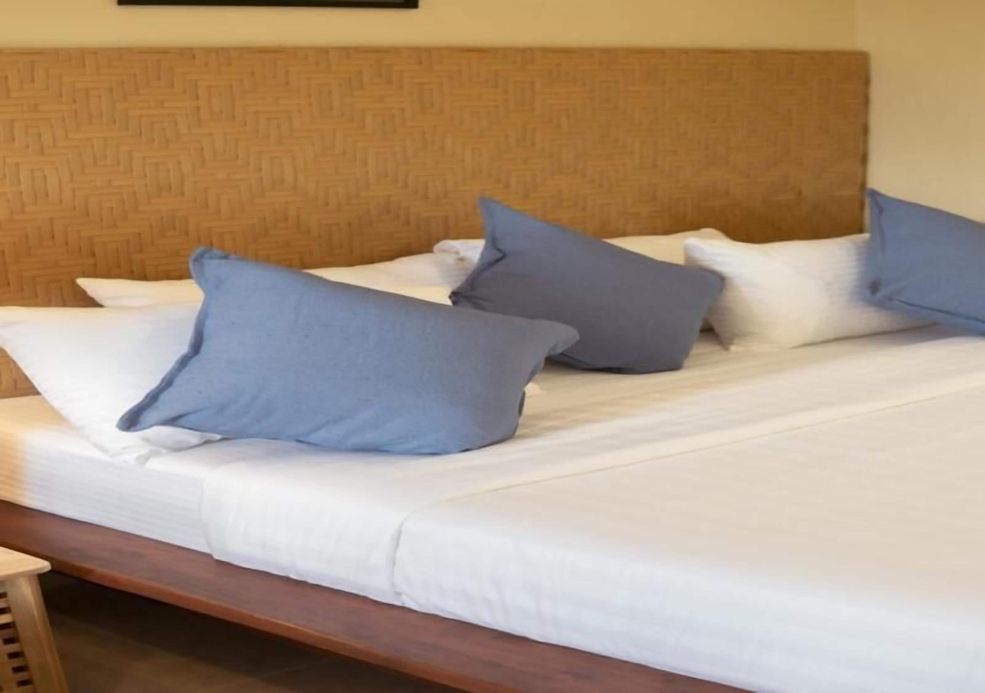 Una cama con cabecera de madera y ropa de cama blanca, adornada con varios almohadones azules.