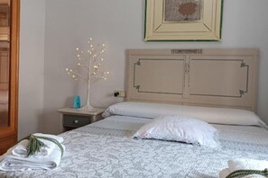 Un lit bien fait, recouvert d’une couvre-lit à motifs, une table de chevet avec une lampe et un tableau encadré accroché au mur.