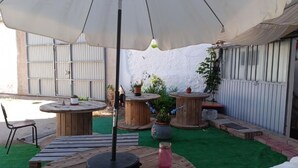 Een terras buiten met ronde houten tafels, een grote parasol en potplanten.