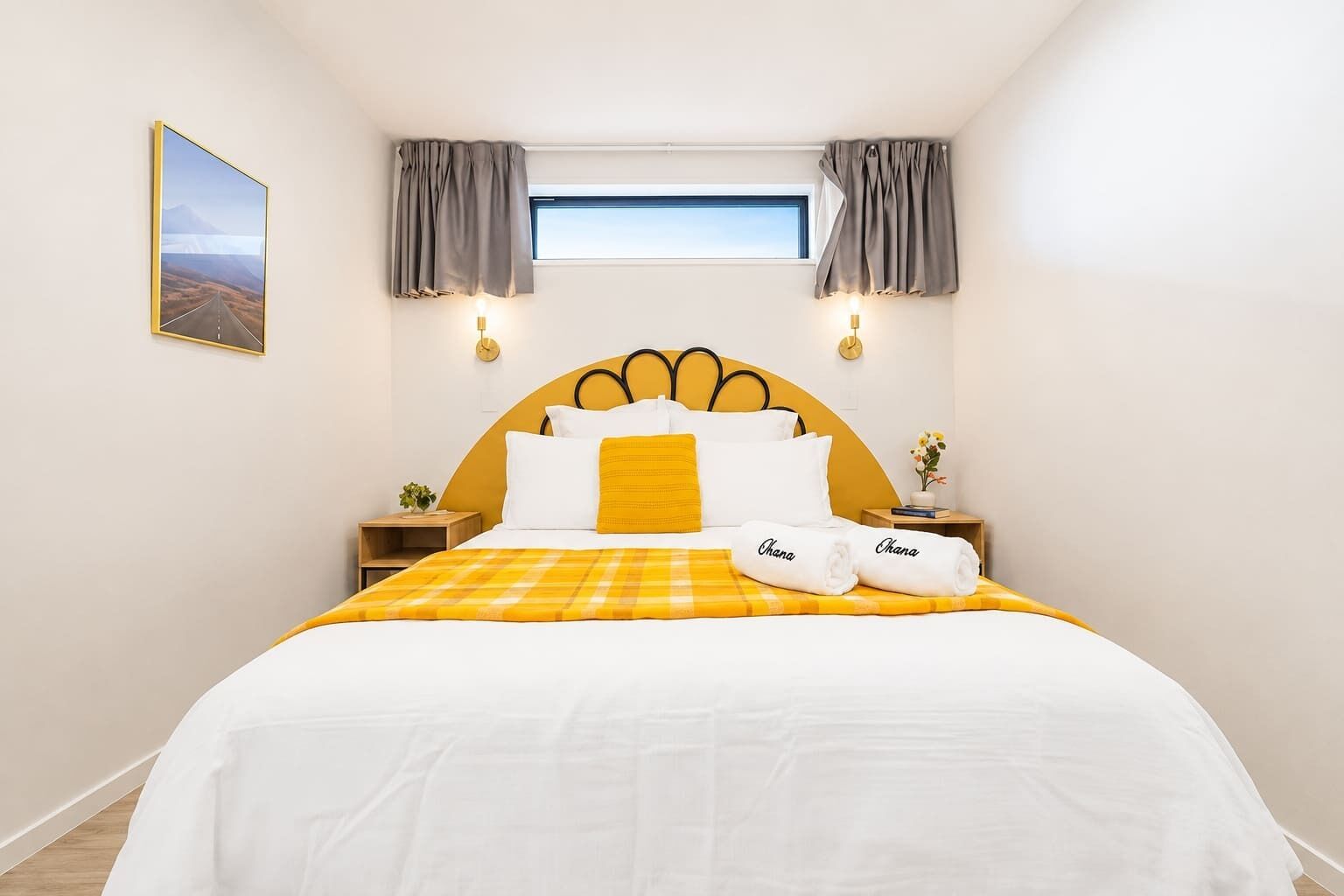 Een hotelkamer met een bed, een nachtkastje met een plant, een raam met gordijnen en een wandklok.