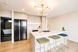 A modern kitchen with a central island, stainless steel appliances, and a unique chandelier. - Christchurch 2BR | Courtyard + Free Parking (Christchurch)