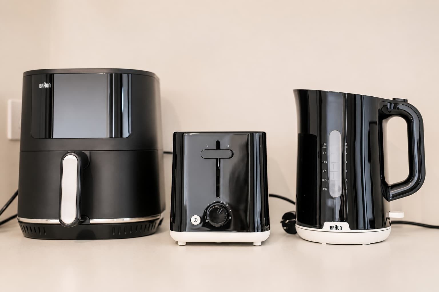 Trois appareils de cuisine noirs : une machine à café, une petite bouilloire électrique et une plus grande bouilloire électrique.