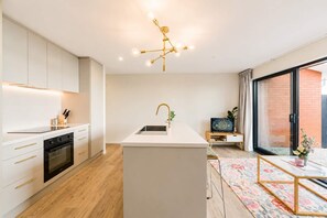 A modern kitchen with a central island, a dining area with a floral rug, and a large sliding glass door to the outside. - Christchurch 2BR | Courtyard + Free Parking (Christchurch)