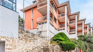 A multi-story building with balconies, a stone staircase, and a green bush.