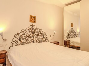 Een opgemaakt bed met een decoratief hoofdeinde, nachtkastjes met lampen en een grote spiegel aan de muur.