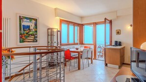 A modern kitchen with a dining area, a staircase with metal railings, and a view of the sea through large windows.