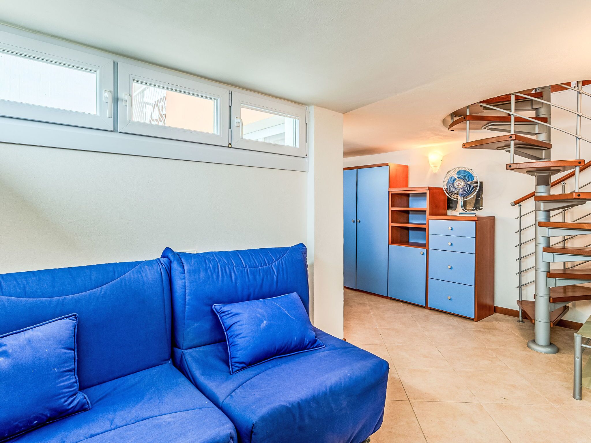 A room with a blue sofa, a wooden spiral staircase, and a wardrobe.