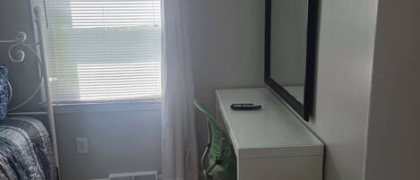 A bedroom with a bed, a desk, a chair, a window with curtains, and a door.