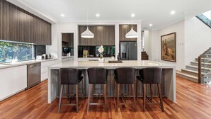 Une cuisine moderne dotée d’un îlot central, de tabourets de bar, de luminaires suspendus et d’un escalier menant à un niveau supérieur.