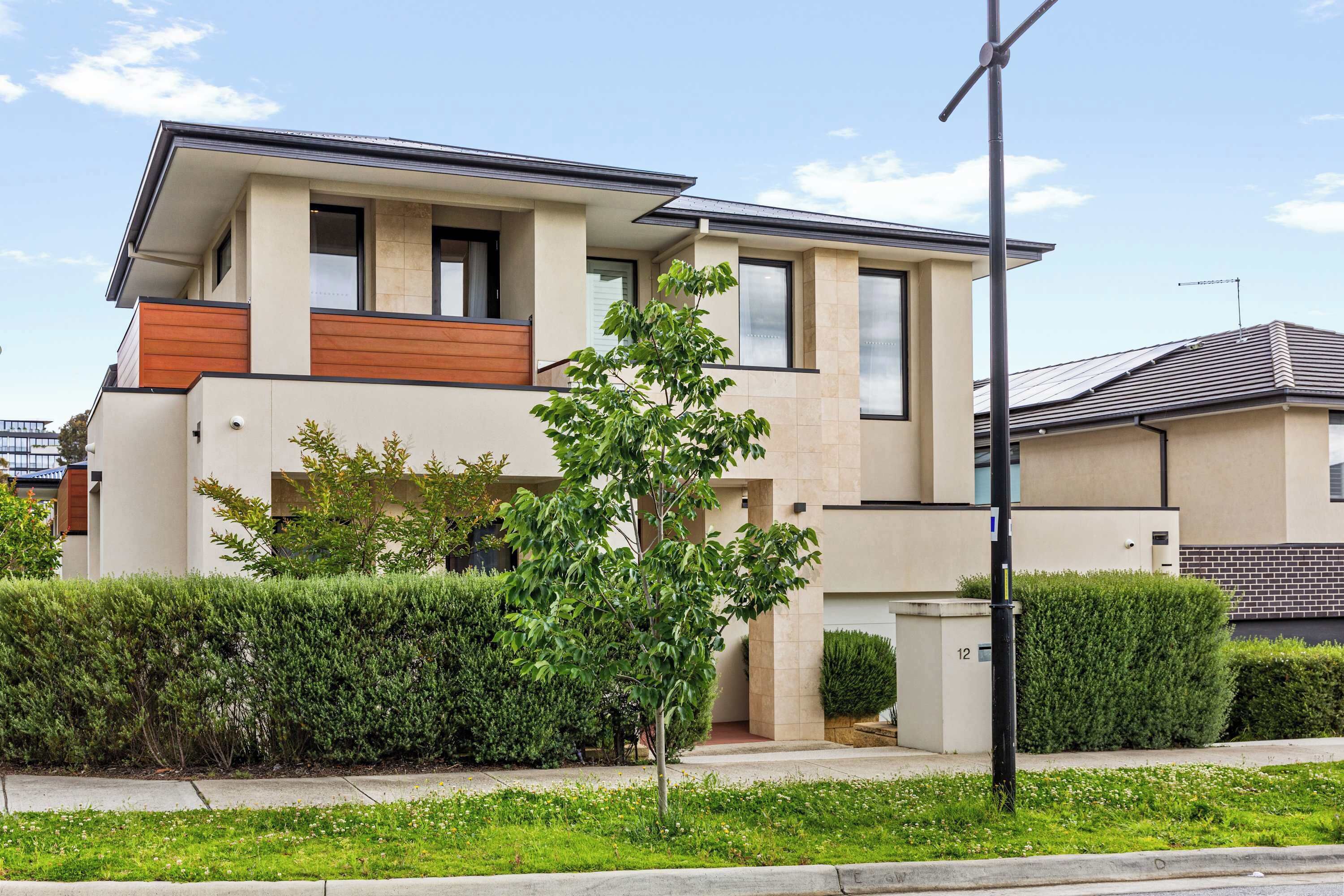 A modern two-story house with a flat roof, large windows, and a small balcony.