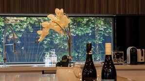 Une cuisine moderne avec un mur en bois, un luminaire suspendu blanc, un vase avec des fleurs blanches et un plateau contenant des bouteilles de vin et des verres.