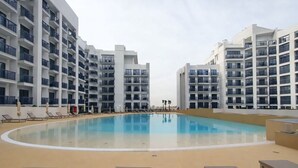 Ett modernt lägenhetskomplex med en central pool, flera balkonger och solstolar.