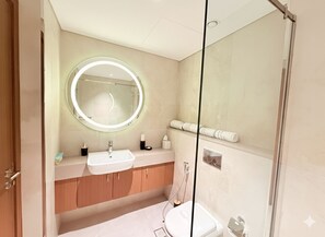 A modern bathroom with a round mirror, a sink, and a toilet. - City Glow Comfort Studio - Oasis Pool (Dubai)