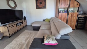 Un salon comprenant un téléviseur, un canapé, un pouf, un meuble en bois et une œuvre d’art accrochée au mur.