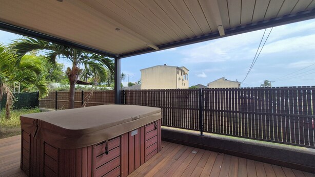 Un espace extérieur abrité doté d’une terrasse en bois, d’un jacuzzi et offrant une vue sur les bâtiments et les palmiers.