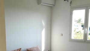 Une chambre à coucher comprenant un lit, des oreillers, une table de chevet avec une lampe, un appareil de climatisation et une fenêtre donnant sur un paysage agréable.