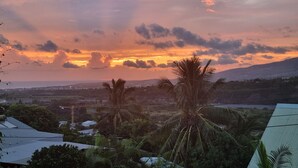Un coucher de soleil sur un paysage parsemé de palmiers et dominé par des collines lointaines.