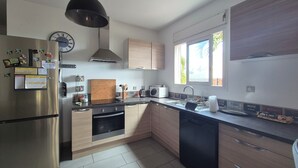 Une cuisine moderne dotée d’appareils électroménagers en acier inoxydable, de meubles en bois, d’un four encastré et d’une fenêtre offrant une vue sur les palmiers.