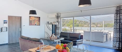 Una cocina moderna con comedor, que incluye una isla grande con fruta y condimentos, un sofá y vistas al exterior.