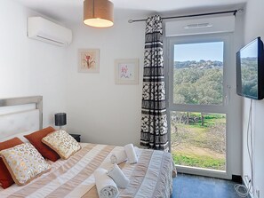 A bedroom with a bed, a TV, a window with a view of the countryside, and a curtain. - La Boétie by Interhome (Porto Vecchio)