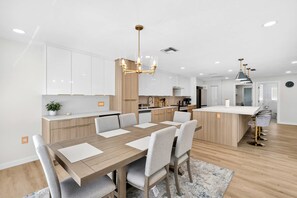 A modern kitchen with white cabinets, a wooden dining table with chairs, and a central island with bar stools. - 4BR Getaway Near Beach & Village  Sleeps 10 (Sarasota)