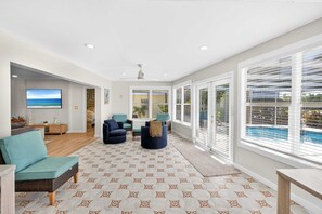 A spacious living area with a patterned floor, a large window with blinds, and a view of a pool. - 4BR Getaway Near Beach & Village  Sleeps 10 (Sarasota)
