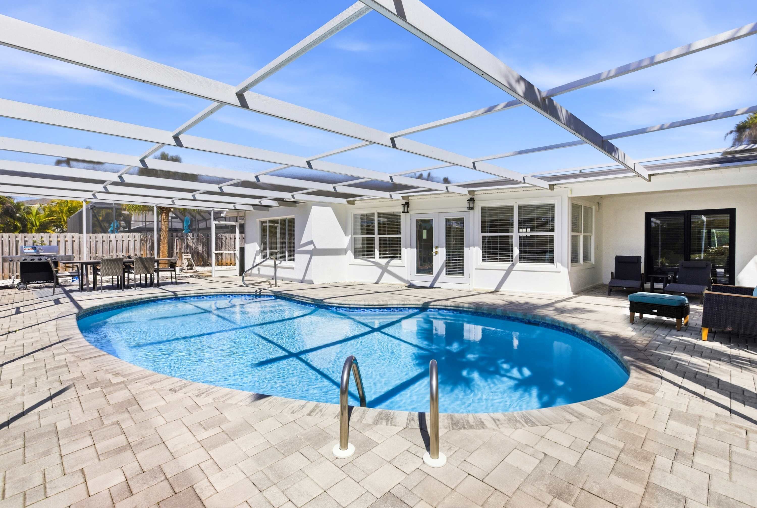 A swimming pool with a glass enclosure, surrounded by a patio area with outdoor furniture and a wooden fence.