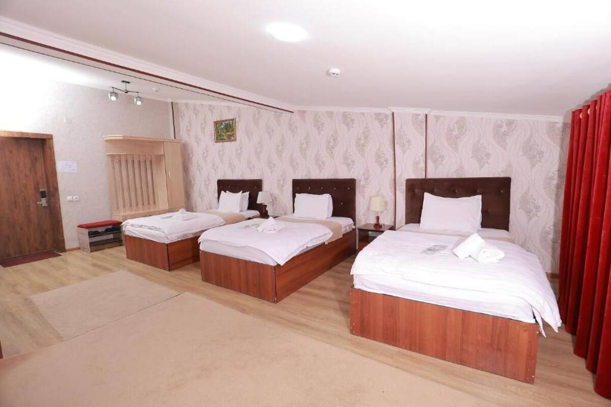 A hotel room with three wooden beds, a wooden wardrobe, a bench, and a small table.