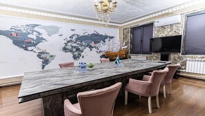 A long dining table with pink chairs, a world map on the wall, and a TV on the wall.