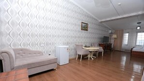 A room with a patterned wallpaper, a sofa, a small table with chairs, a television, and a bed.