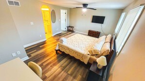 Un dormitorio con cama, escritorio, silla, ventilador de techo, televisor y ventana con persianas.