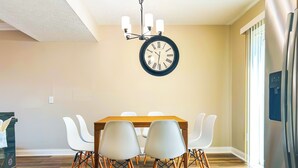 Un comedor con una mesa de madera, sillas blancas y un reloj de pared.