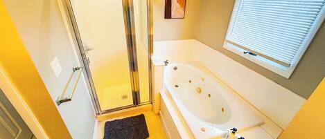 A bathroom with a shower, a bathtub, and a window with blinds.