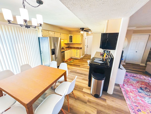 Cocina compacta con refrigerador, microondas y estufa. Hay una zona de comedor con mesa y sillas. El cuarto tiene piso de madera y un ventilador de techo.