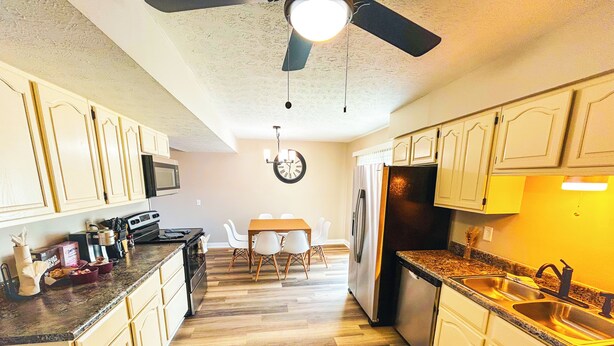 Una cocina con armarios de madera, un refrigerador, un microondas y un comedor con mesa y sillas.