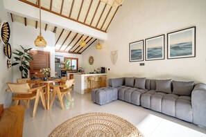 Una sala de estar moderna con un sofá seccional gris, una mesa de comedor de madera y una cocina al fondo.