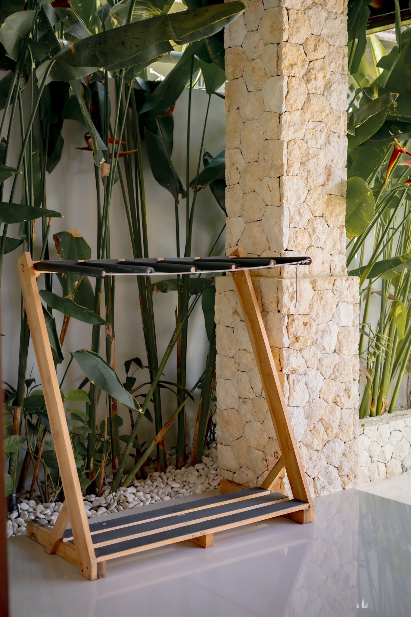 A wooden swing set against a stone wall with tropical plants.