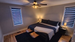 Ein Schlafzimmer mit einem Bett, einem Deckenventilator, zwei Nachttischlampen, einem schwarzen Teppich und Holzdielen.