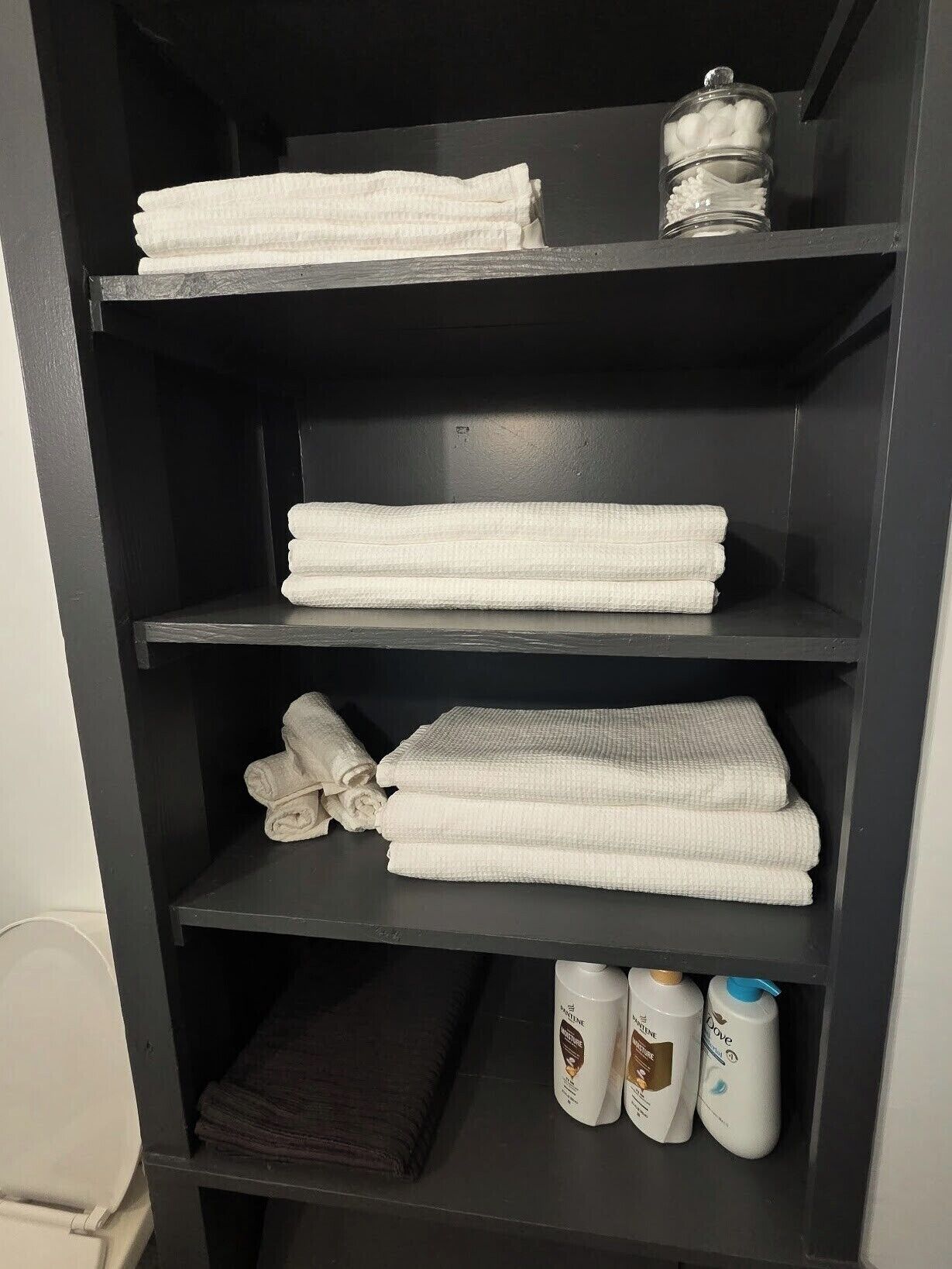 Une étagère noire sur laquelle sont pliés soigneusement des serviettes blanches, ainsi que deux flacons de produits de toilette.