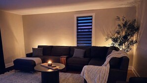 Un salon chaleureux avec un canapé aux couleurs sombres, une table basse ronde et une petite table d’appoint.