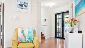 Um interior moderno com uma poltrona amarela, almofada com padrão de cactos, pintura oceânica emoldurada e uma porta de vidro que dá para uma escada.