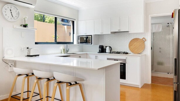 Uma cozinha moderna com armários brancos, uma ilha grande com banquetas, micro-ondas e cafeteira.