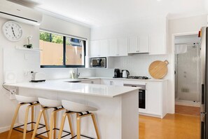 Una cocina moderna con armarios blancos, una isla grande con taburetes de bar, un microondas y una cafetera.