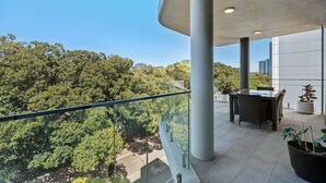 A balcony with a glass railing, a dining table with chairs, and a potted plant. - South Perth Sky - Foreshore Escape (Perth)