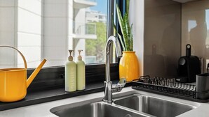 A modern kitchen with a stainless steel sink, a yellow pot, two green bottles, and a yellow vase. - South Perth Sky - Foreshore Escape (Perth)
