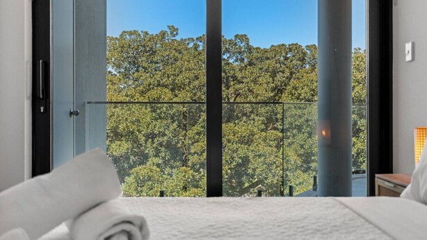 A bedroom with a large window, a bed, and a view of trees. - South Perth Sky - Foreshore Escape (Perth)