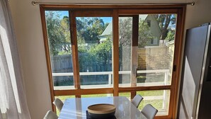 A dining area with a white table, six chairs, a wooden bowl, and a view through large windows to a backyard. - Island Getaway on Bay - Pet friendly - Wifi - Winter special 4th night free (Cowes)