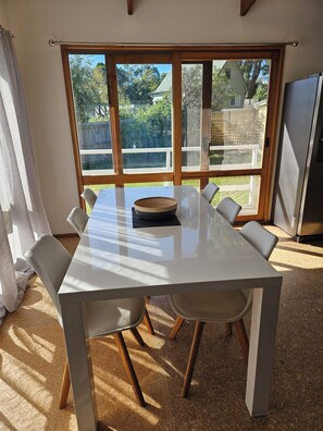 A dining area with a white table, six chairs, a wooden bowl, and a view through large windows to a backyard. - Island Getaway on Bay - Pet friendly - Wifi - Winter special 4th night free (Cowes)