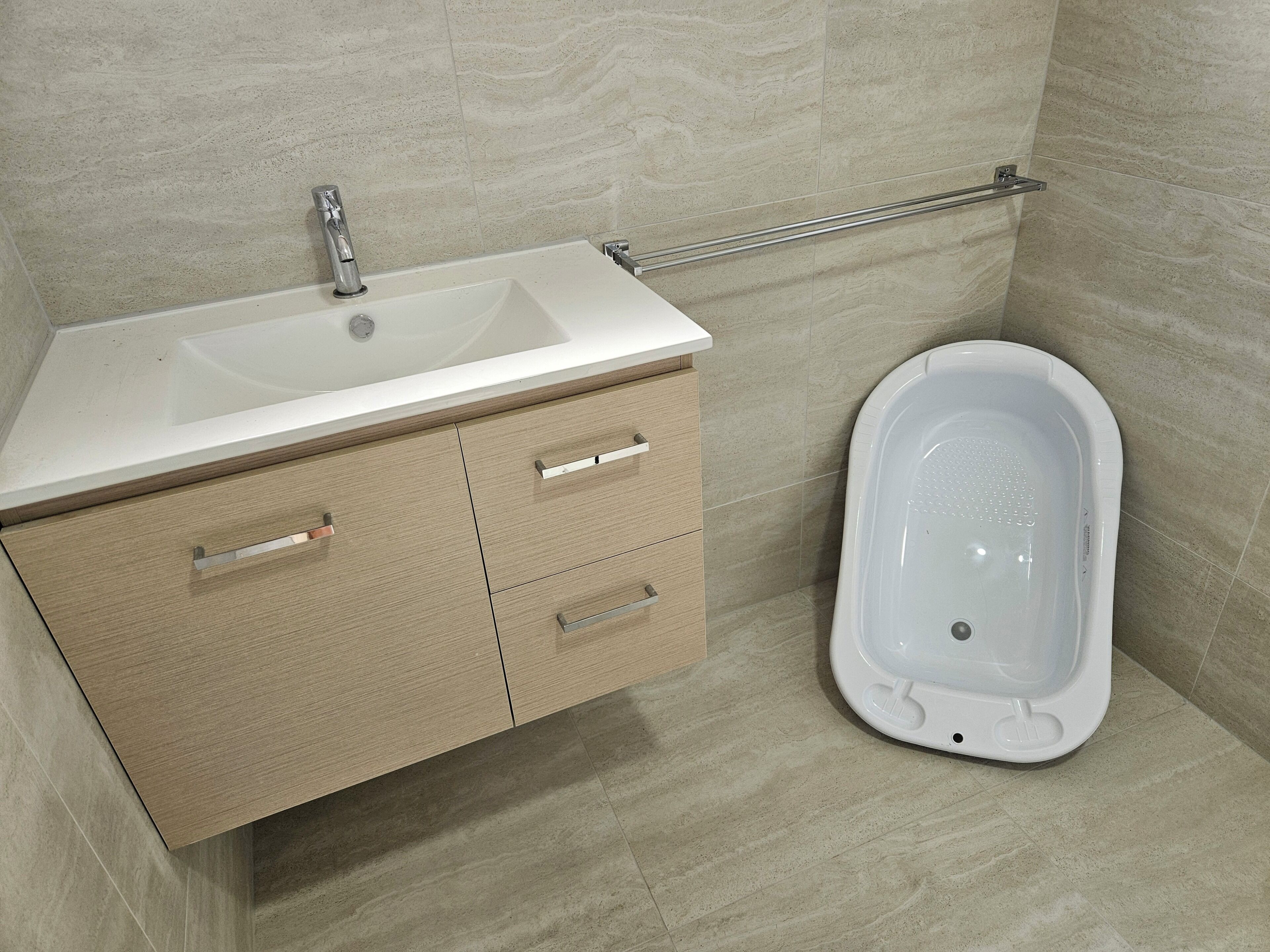 Un baño con lavamanos blanco, mueble de madera y bañera blanca.