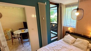 A bedroom with a bed, a table with chairs, a window with curtains, and a radiator. - Le Pradet A 781 - Mont Dore 4 Pers (Mont-Dore)